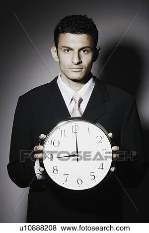 Stock Photo - Portrait of a businessman holding a clock. Fotosearch