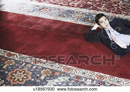 Stock Image - Portrait of a businessman lying on a carpet listening to an MP3 player. Fotosearch
