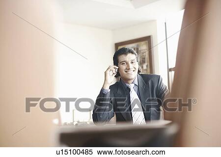 Stock Photography - Portrait of a businessman sitting in an office talking on a mobile phone. Fotosearch