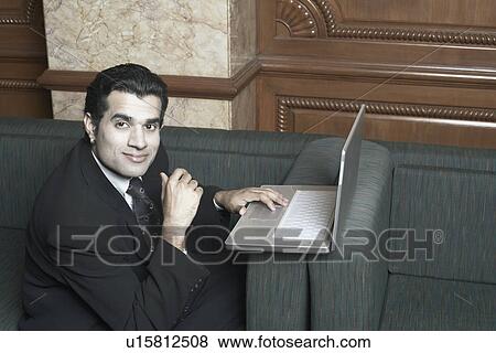 Portrait of a businessman sitting on a couch with a laptop View Large Photo Image Stock Photo - Portrait of a businessman sitting on a couch with a laptop. Fotosearch