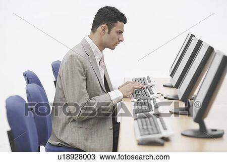 Stock Image - Side profile of a businessman sitting in front of a computer. Fotosearch