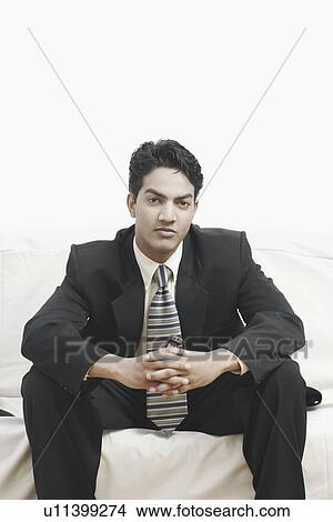 Picture - Portrait of a businessman sitting on a couch holding a mobile phone. Fotosearch