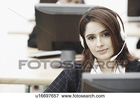 Portrait of a businesswoman wearing a headset sitting in front of a computer View Large Photo Image Stock Photo - Portrait of a businesswoman wearing a headset sitting in front of a computer. Fotosearch