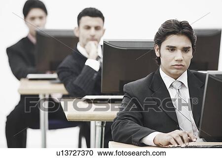 Stock Image - Three businessmen working on computers in an office. Fotosearch