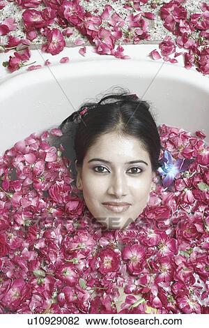 Stock Image - High angle view of a young woman lying in a bathtub covered with flower petals. Fotosearch