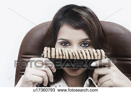 Stock Image - Portrait of a businesswoman holding cookies in front of her face. Fotosearch