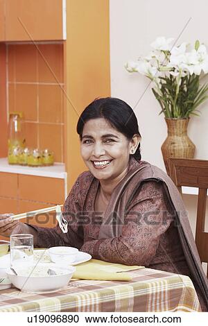 Stock Image - Portrait of a mature woman eating noodles with chopsticks. Fotosearch