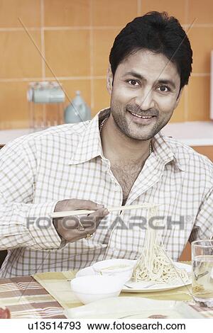 Stock Image - Portrait of a mid adult man holding noodles with a pair of chopsticks. Fotosearch