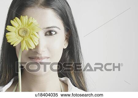 Stock Photography - Portrait of a young woman with a flower in front of her face. Fotosearch