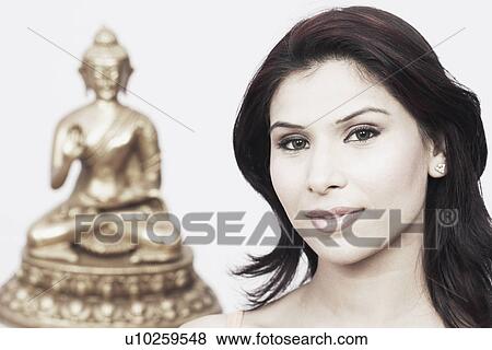 Portrait of a young woman with a statue of Buddha behind her View Large Photo Image Stock Photo - Portrait of a young woman with a statue of Buddha behind her. Fotosearch