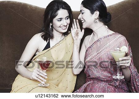 Stock Image - Close-up of a young woman whispering into another young woman's ear. Fotosearch