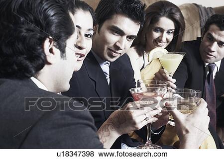 Stock Photo - Close-up of three young men and two young women raising a toast with martini and whiskey glasses. Fotosearch