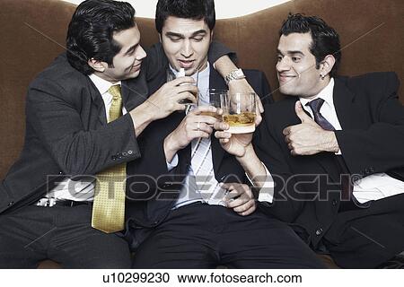Stock Image - Close-up of three young men holding glasses of whiskey. Fotosearch