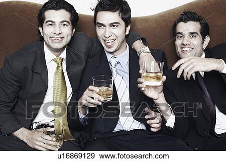 Stock Photo - Close-up of three young men holding glasses of whiskey. Fotosearch