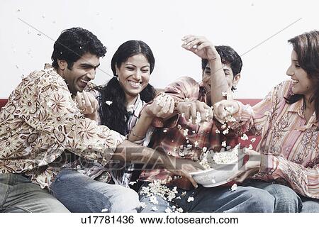 Stock Photograph - Close-up of two young couples sitting together on a couch eating popcorn. Fotosearch