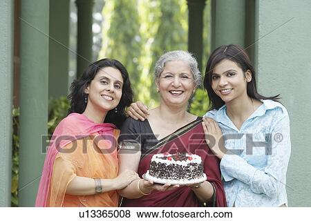 Portrait of a mature woman holding a cake with a young woman and a mid adult woman standing beside her View Large Photo Image Stock Photo - Portrait of a mature woman holding a cake with a young woman and a mid adult woman standing beside her. Fotosearch