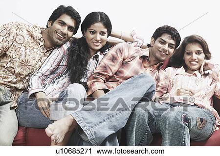 Stock Image - Portrait of two young couples sitting together on a couch and smiling. Fotosearch