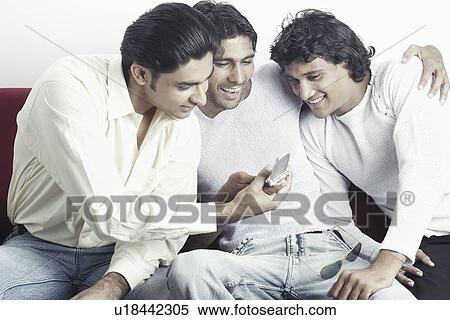 Three young men looking at a mobile phone View Large Photo Image Stock Photography - Three young men looking at a mobile phone. Fotosearch