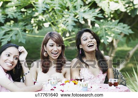 Stock Image - Two young women and a teenage girl sitting at a table and laughing. Fotosearch