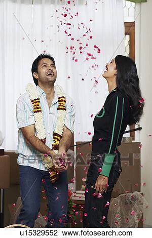 Stock Image - Close-up of a young couple laughing with rose petals falling on them. Fotosearch