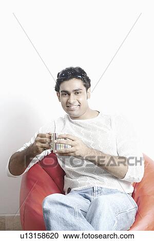 Portrait of a young man holding a mug sitting on a bean bag View Large Photo Image Stock Image - Portrait of a young man holding a mug sitting on a bean bag. Fotosearch