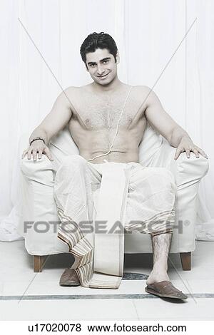 Stock Photo - Portrait of a young man sitting on an armchair wearing traditional clothing. Fotosearch