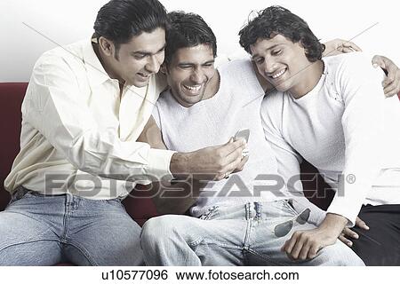 Three young men looking at a mobile phone View Large Photo Image Stock Photograph - Three young men looking at a mobile phone. Fotosearch