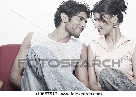 Stock Photo - Young couple sitting on a couch looking at each other. Fotosearch