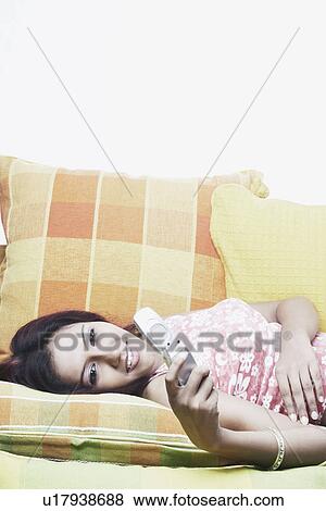 Stock Photo - Young woman lying on a couch and holding a mobile phone. Fotosearch