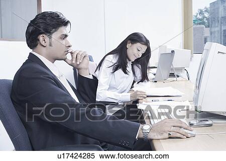Stock Photography - Businessman and a businesswoman sitting in an office. Fotosearch