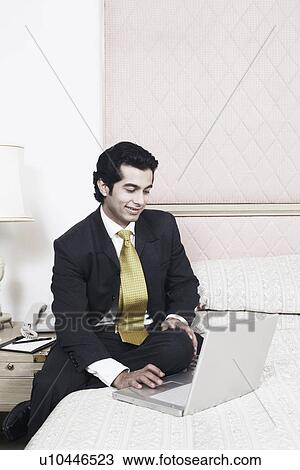 Businessman sitting on the bed using a laptop View Large Photo Image Stock Image - Businessman sitting on the bed using a laptop. Fotosearch