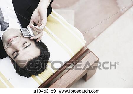 Stock Photo - High angle view of a businessman lying on the bed talking on a mobile phone. Fotosearch