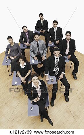 Stock Photo - High angle view of business executives sitting on chairs with mobile phones. Fotosearch