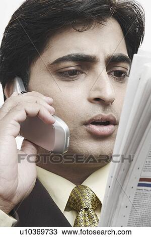 Low angle view of a businessman reading a newspaper and talking on a mobile phone View Large Photo Image Stock Image - Low angle view of a businessman reading a newspaper and talking on a mobile phone. Fotosearch