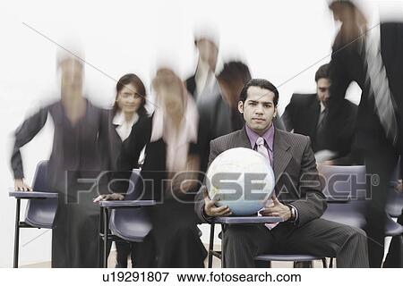 Stock Photo - Portrait of a businessman sitting in a meeting holding a globe. Fotosearch