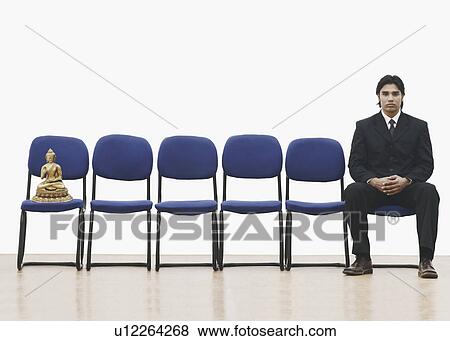 Portrait of a businessman sitting on a chair with a statue of Buddha on a chair beside him View Large Photo Image Stock Photo - Portrait of a businessman sitting on a chair with a statue of Buddha on a chair beside him. Fotosearch
