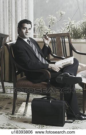 Stock Photograph - Portrait of a businessman sitting on an armchair holding a newspaper. Fotosearch