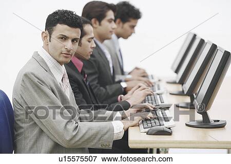Stock Photo - Side profile of four businessmen sitting in front of computers. Fotosearch