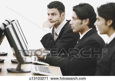 Stock Image - Side profile of three businessmen working on computers in an office. Fotosearch