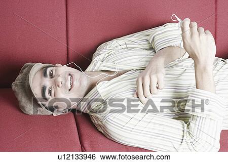 High angle view of a young man lying on a couch and listening to an MP3 player View Large Photo Image Stock Photograph - High angle view of a young man lying on a couch and listening to an MP3 player. Fotosearch