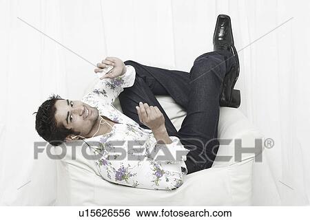 Stock Photograph - High angle view of a young man lying on an armchair listening to an MP3 player. Fotosearch