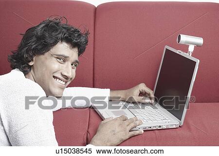 Portrait of a young man sitting in front of a laptop View Large Photo Image Stock Photography - Portrait of a young man sitting in front of a laptop. Fotosearch