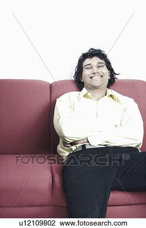 Stock Image - Portrait of a young man sitting on a couch. Fotosearch