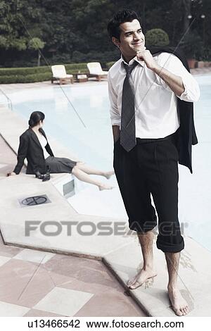 Young man standing near a swimming pool with a young woman sitting behind him View Large Photo Image Stock Image - Young man standing near a swimming pool with a young woman sitting behind him. Fotosearch