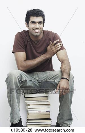 Portrait of a young man sitting on a stack of books View Large Photo Image Stock Photo - Portrait of a young man sitting on a stack of books. Fotosearch