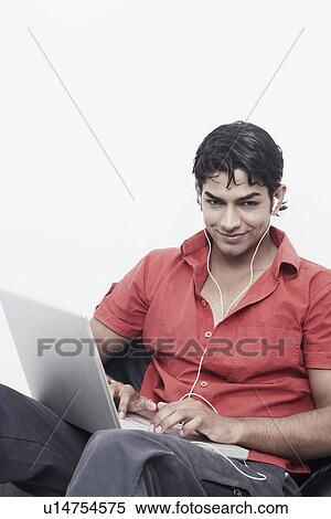 Portrait of a young man wearing headphones using a laptop View Large Photo Image Stock Photography - Portrait of a young man wearing headphones using a laptop. Fotosearch