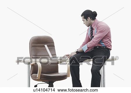 Picture - Side profile of a businessman sitting on a table working on a laptop. Fotosearch