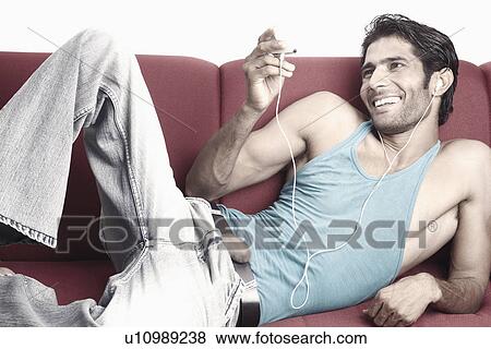 Stock Photo - Young man lying on a couch listening to an MP3 Player. Fotosearch