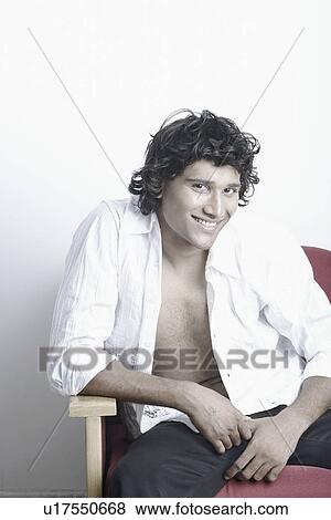 Young man sitting on a couch smiling View Large Photo Image Stock Photo - Young man sitting on a couch smiling. Fotosearch