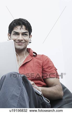 Low angle view of a young man wearing headphones using a laptop View Large Photo Image Stock Image - Low angle view of a young man wearing headphones using a laptop. Fotosearch